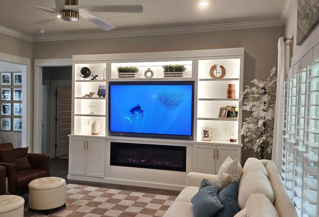 Custom white built-in entertainment center with LED-lit shelves, electric fireplace, and wall-mounted TV